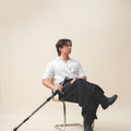 A man sitting on a chair wearing Werable's easy grip buckle shirt with black Hakama culottes pants holding onto a crutch.