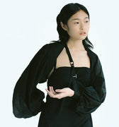 Woman in Werable's black transformable bolero, slung as an arm sling, posing.