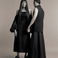 Woman in Werable's cross back dress and transformable bolero in black, holding hands with a man in a sleeveless top and Werable's hakama full length pants in black.