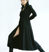 Woman in a black Werable easy grip buckle wrap dress and black boots, posing with one leg extended.
