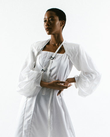 Woman in Werable's bolero in an arm sling and wrap dress in white.