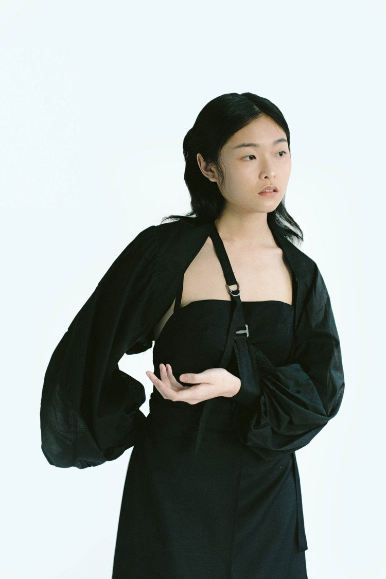 Woman in Werable's black transformable bolero, slung as an arm sling, posing.