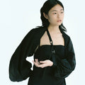 Woman in Werable's black transformable bolero, slung as an arm sling, posing.