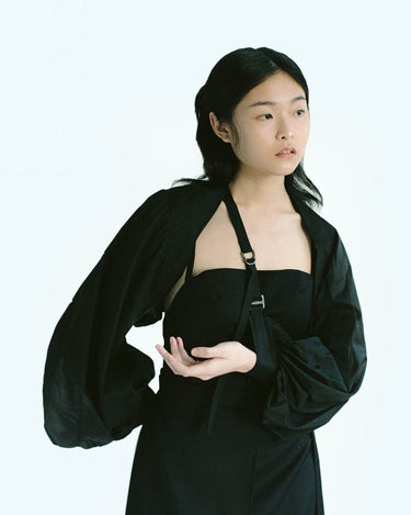 Woman in Werable's black transformable bolero, slung as an arm sling, posing.