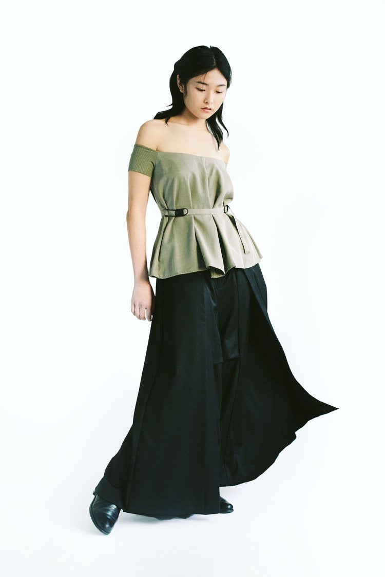 Front view of a woman wearing Werable's sage green off shoulder top with Hakama full length pants in black. 