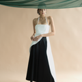 Asian woman in matisse halter top in white with hakama culottes in black and boots, standing under draped green fabric.