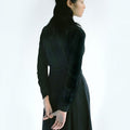 Back view of a woman in Werable's black easy grip buckle shirt dress with hands clasped behind her.