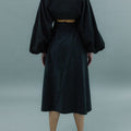 Back view of woman wearing transformable bolero and cross-back dress in black.